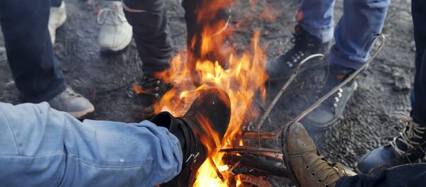 Migrants warm themselves by a fire while waiting for a train to Croatia at a train station in Presevo, Serbia, January 20, 2016 - Sputnik International
