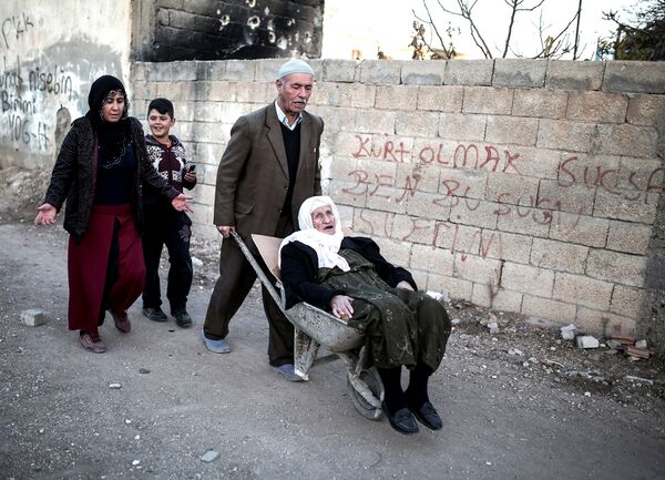 A man wheels a sick person in a wheelbarrow through the barricades set up by the militants of the Kurdistan Workers' Party, or PKK, in Nusaybin, Turkey, Thursday, Dec. 24, 2015.  - Sputnik International