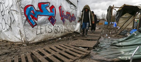 Migrants walk among tents in a muddy field at a camp of makeshift shelters for migrants and asylum-seekers from Iraq, Kurdistan, Iran and Syria, called the Grande Synthe jungle, near Calais, France - Sputnik International