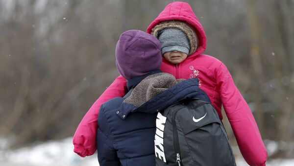 A migrant carries a child as they walk through a frozen field after crossing the border from Macedonia, near the village of Miratovac, Serbia, January 18, 2016. - Sputnik International