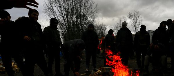 Migrants try to warm up around a brazier in a muddy field at a camp of makeshift shelters. Migrants try to warm up around a brazier in a muddy field at a camp of makeshift shelters. - Sputnik International