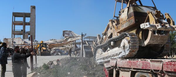 A bulldozer is unloaded from a truck as people gather around the rubble of a hospital supported by Doctors Without Borders (MSF) near Maaret al-Numan, in Syria's northern province of Idlib, on February 15, 2016 - Sputnik International