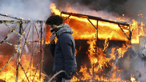 A migrant walks past a burning makeshift shelter set ablaze in protest against the partial dismantlement of the camp for migrants. - Sputnik International