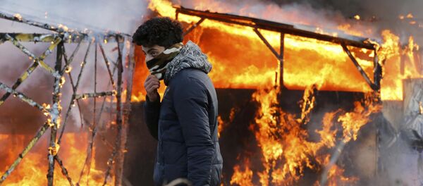 A migrant walks past a burning makeshift shelter set ablaze in protest against the partial dismantlement of the camp for migrants. - Sputnik International