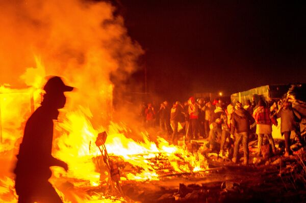 Migrants stand next a fire burning shacks, in the southern part of the so-called Jungle migrant camp, as half of the camp is being dismantled, in the French northern port city of Calais, on March 1, 2016. - Sputnik International