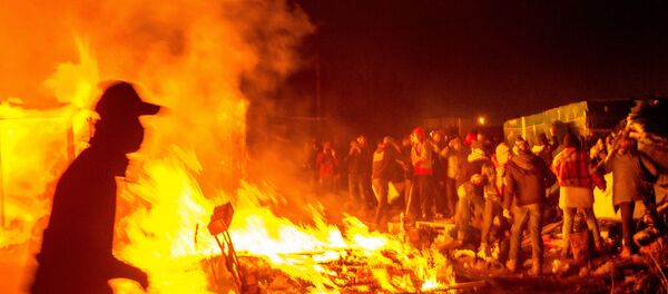 Migrants stand next a fire burning shacks, in the southern part of the so-called Jungle migrant camp, as half of the camp is being dismantled, in the French northern port city of Calais, on March 1, 2016. Migrants stand next a fire burning shacks, in the southern part of the so-called Jungle migrant camp, as half of the camp is being dismantled, in the French northern port city of Calais, on March 1, 2016. - Sputnik International