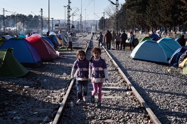 Sisters walk on railway tracks where refugees installed their tents at the makeshift camp of the Greek-Macedonian border near the Greek village of Idomeni, on March 5, 2016, where thousands of refugees and migrants wait to cross the border into Macedonia Sisters walk on railway tracks where refugees installed their tents at the makeshift camp of the Greek-Macedonian border near the Greek village of Idomeni, on March 5, 2016, where thousands of refugees and migrants wait to cross the border into Macedonia - Sputnik International