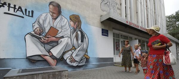 Women with children walk past graffiti showing Russian President Vladimir Putin, dressed in a Judogi and sitting next to a girl, on the front of a children's clinic in Yalta, Crimea, Wednesday, Aug. 19, 2015 - Sputnik International