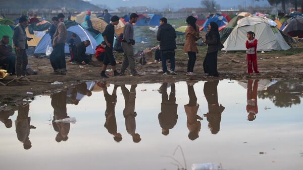 Migrants are reflected in a puddle at the northern Greek border station of Idomeni, Tuesday, March 8, 2016. - Sputnik International