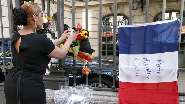 A woman leaves a bouquet of flowers in the Belgian national colours next to a French national flag with the lettering 'Paris - Brussels - Solidarity' at the fence of the Belgian embassy in Paris on March 22, 2016 - Sputnik International