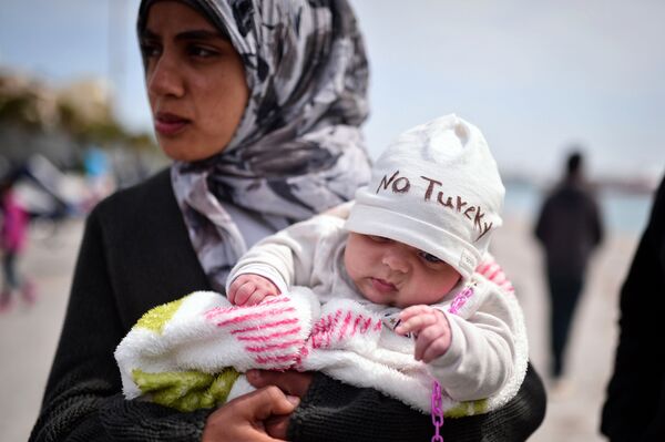 A Syrian refugee holds a two-month old baby as refugees and migrants who broke out from Chios detention camp, and camped out in the port of the city, stage a protest with their children chanting 'No Turkey' on April 3, 2016. - Sputnik International