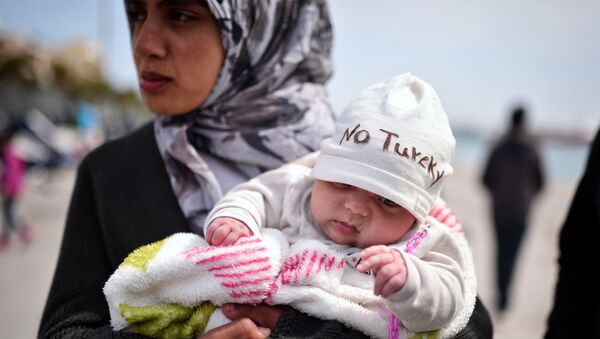 A Syrian refugee holds a two-month old baby as refugees and migrants who broke out from Chios detention camp, and camped out in the port of the city, stage a protest with their children chanting 'No Turkey' on April 3, 2016. - Sputnik International