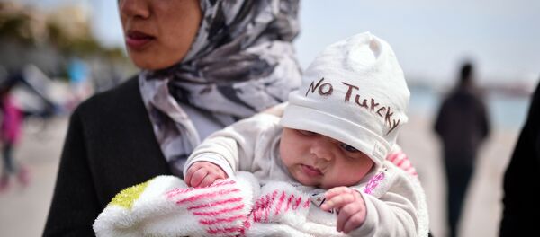 A Syrian refugee holds a two-month old baby as refugees and migrants who broke out from Chios detention camp, and camped out in the port of the city, stage a protest with their children chanting 'No Turkey' on April 3, 2016. - Sputnik International