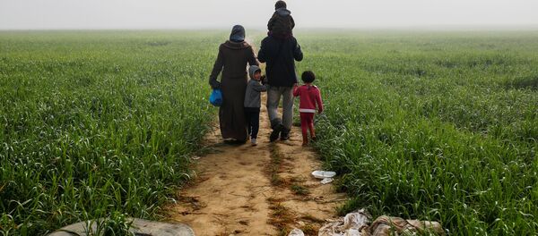 A family walks through a field at a makeshift camp for migrants and refugees at the Greek-Macedonian border near the village of Idomeni, Greece, April 4, 2016. A family walks through a field at a makeshift camp for migrants and refugees at the Greek-Macedonian border near the village of Idomeni, Greece, April 4, 2016. - Sputnik International