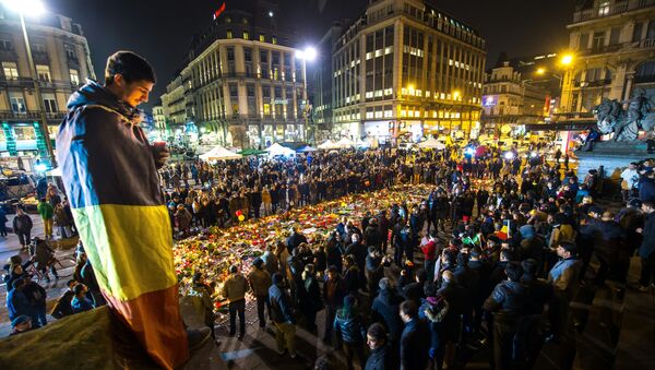 A man wrapped in a Belgian flag holds a candle as people gather at a makeshift memorial in front of Brussel's Stock Exchange on Place de la Bourse (Beursplein) on March 24, 2016 - Sputnik International