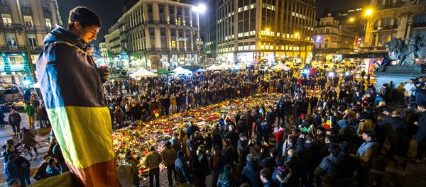 A man wrapped in a Belgian flag holds a candle as people gather at a makeshift memorial in front of Brussel's Stock Exchange on Place de la Bourse (Beursplein) on March 24, 2016 - Sputnik International