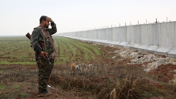 A Kurdish People's Protection Unit(YPG) fighter stands near a wall which activists say was put up by Turkish authorities, on the Syria-Turkey border in the western Syrian countryside of Ras al-Ain on February 2, 2016 - Sputnik International