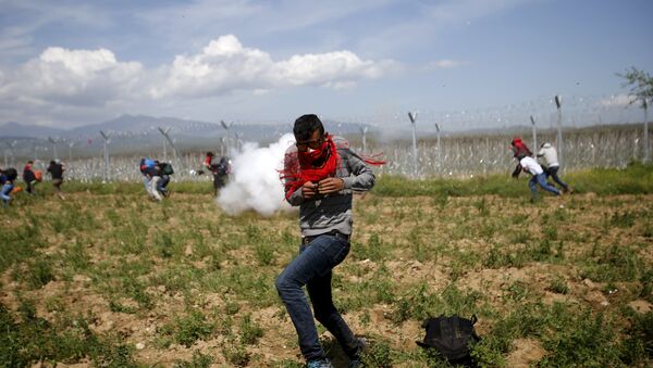 A migrant flees from teargas smoke thrown by Macedonian police on a crowd of more than 500 refugees and migrants protesting next to a border fence at a makeshift camp at the Greek-Macedonian border near the village of Idomeni, Greece - Sputnik International