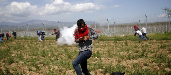 A migrant flees from teargas smoke thrown by Macedonian police on a crowd of more than 500 refugees and migrants protesting next to a border fence at a makeshift camp at the Greek-Macedonian border near the village of Idomeni, Greece - Sputnik International