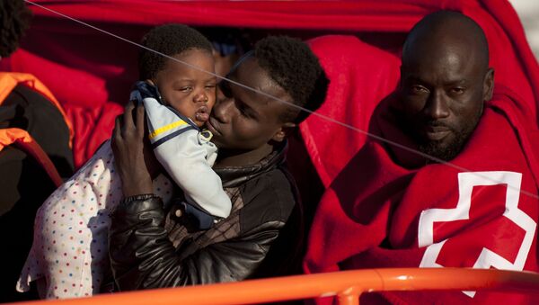 A migrants wrapped in a red cross blanket holds a child on arrival into the southern Spanish port of Malaga on January 27, 2016 after an inflatable boat carrying 55 Africans, seven of them women and six chidren, was rescued by the Spanish coast guard off the Spanish coast (File) - Sputnik International