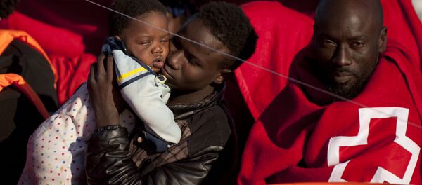 A migrants wrapped in a red cross blanket holds a child on arrival into the southern Spanish port of Malaga on January 27, 2016 after an inflatable boat carrying 55 Africans, seven of them women and six chidren, was rescued by the Spanish coast guard off the Spanish coast (File) A migrants wrapped in a red cross blanket holds a child on arrival into the southern Spanish port of Malaga on January 27, 2016 after an inflatable boat carrying 55 Africans, seven of them women and six chidren, was rescued by the Spanish coast guard off the Spanish coast (File) - Sputnik International
