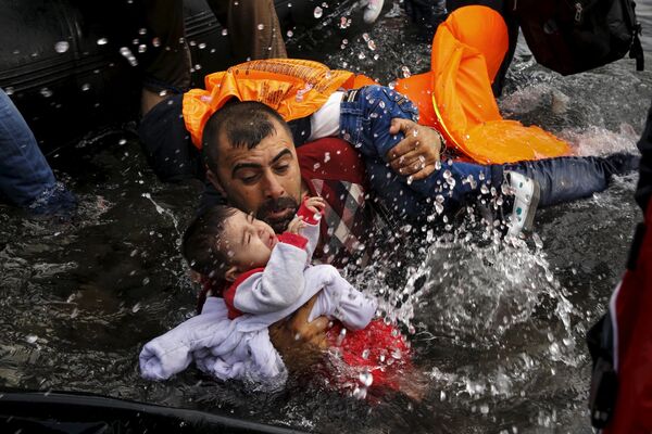 A Syrian refugee holds onto his children as he struggles to walk off a dinghy on the Greek island of Lesbos, after crossing a part of the Aegean Sea from Turkey to Lesbos. file photo A Syrian refugee holds onto his children as he struggles to walk off a dinghy on the Greek island of Lesbos, after crossing a part of the Aegean Sea from Turkey to Lesbos. file photo - Sputnik International