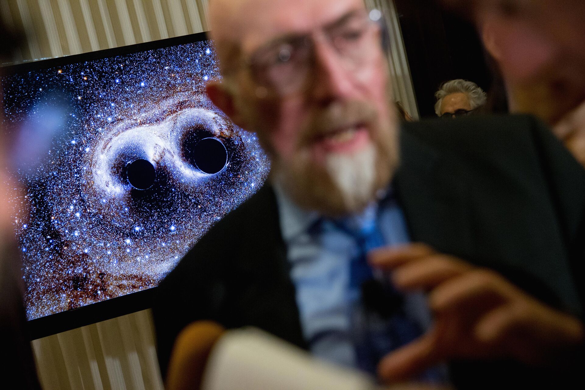  visual of gravitational waves from two converging black holes is depicted on a monitor behind Laser Interferometer Gravitational-Wave Observatory (LIGO) Co-Founder Kip Thorne as he speaks to members of the media following a news conference at the National Press Club in Washington, Thursday, Feb. 11, 2016 - Sputnik International, 1920, 09.11.2021