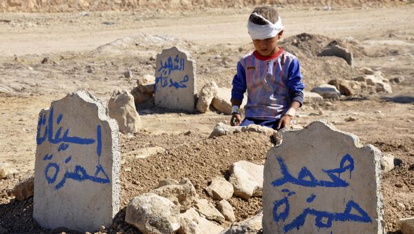Ali Hamza, 8, sits at the graves of his brother, Mohammed, and sister Asinat, who were killed in a suicide car bomb attack in the Shiite Turkmen village of Qabak near Tal Afar. file photo - Sputnik International