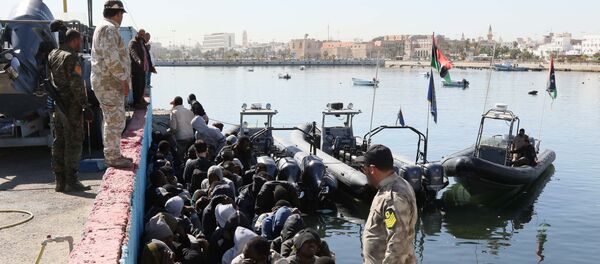 Illegal migrants sit on the dock at the Tripoli port after 115 migrants of African origins were rescued by two coast guard boats at sea when their boat started sinking off the Libyan coast on April 11, 2016 - Sputnik International