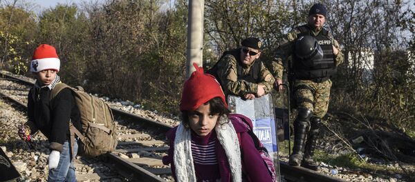 Police officers watch two children walk past as migrants and refugees cross the Greek-Macedonian border near the town of Gevgelija, Macedonia (File) - Sputnik International
