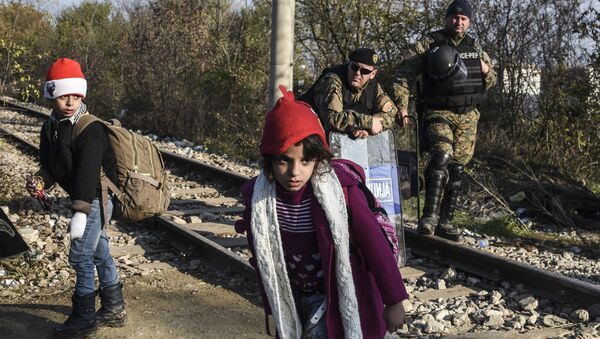 Police officers watch two children walk past as migrants and refugees cross the Greek-Macedonian border near the town of Gevgelija, Macedonia (File) - Sputnik International