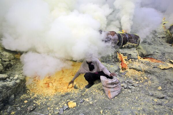 In this April 16, 2016 photo, volcanic smoke blankets a miner as he collects sulfur rocks he just dug up at the crater of Mount Ijen in Banyuwangi, East Java, Indonesia In this April 16, 2016 photo, volcanic smoke blankets a miner as he collects sulfur rocks he just dug up at the crater of Mount Ijen in Banyuwangi, East Java, Indonesia - Sputnik International