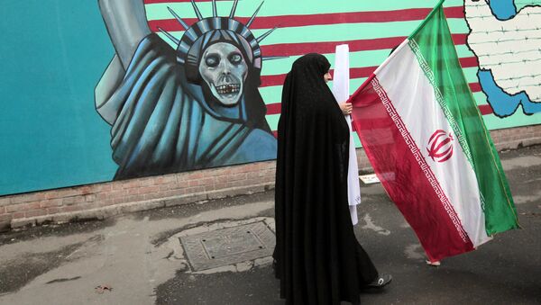 An Iranian woman holds her national flag as she walks past an anti-US mural depicting the Statue of Liberty on the wall of the former US embassy in Tehran (File) - Sputnik International