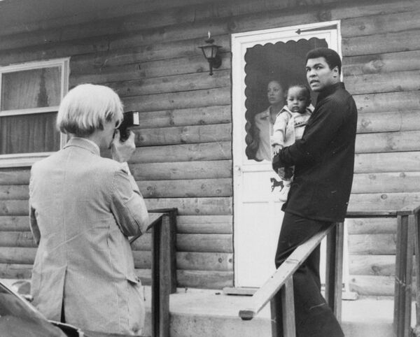Pop artist Andy Warhol, left, is shown photographing Muhammad Ali, his infant daughter, Hanna, and wife, Veronica, Thursday, August 18, 1977, at Ali's training camp in Deer Lake, Pa. - Sputnik International