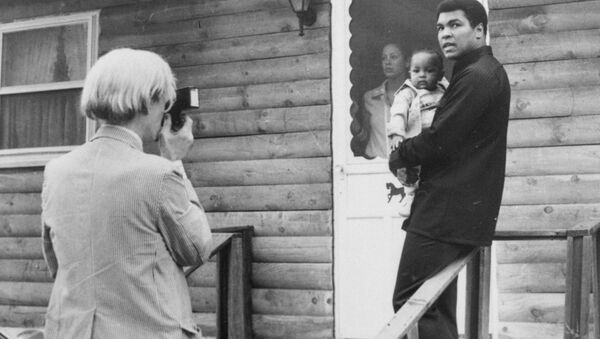 Pop artist Andy Warhol, left, is shown photographing Muhammad Ali, his infant daughter, Hanna, and wife, Veronica, Thursday, August 18, 1977, at Ali's training camp in Deer Lake, Pa. - Sputnik International