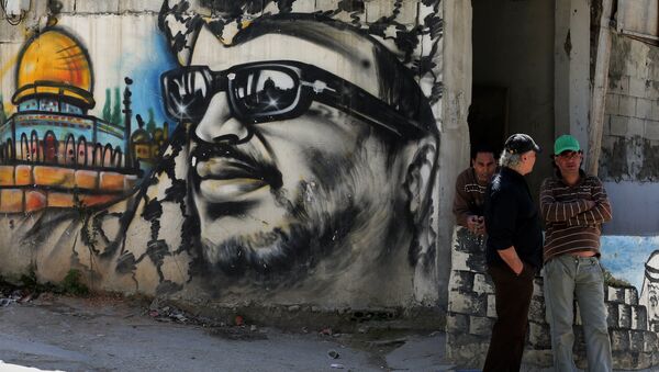 Palestinian refugees stand next to graffiti bearing a portrait of late Palestinian President Yasser Arafat at the Ain Al-Helweh refugee camp, near the southern Lebanese city of Sidon, on March 16, 2015 - Sputnik International