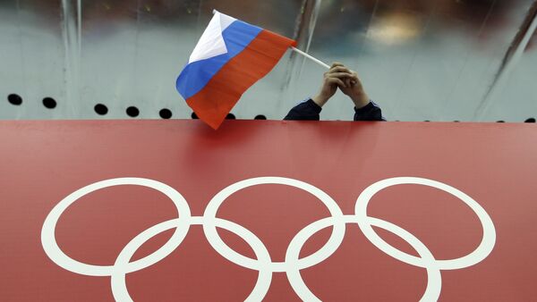 In this Feb. 18, 2014 file photo, a Russian skating fan holds the country's national flag over the Olympic rings before the start of the men's 10,000-meter speedskating race at Adler Arena Skating Center during the 2014 Winter Olympics in Sochi, Russia - Sputnik International
