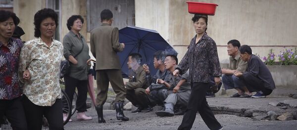 A North Korean woman balances a pail on her head while she walks past men smoking by the road at the end of a work day on Wednesday, June 22, 2016, in Wonsan, North Korea. - Sputnik International