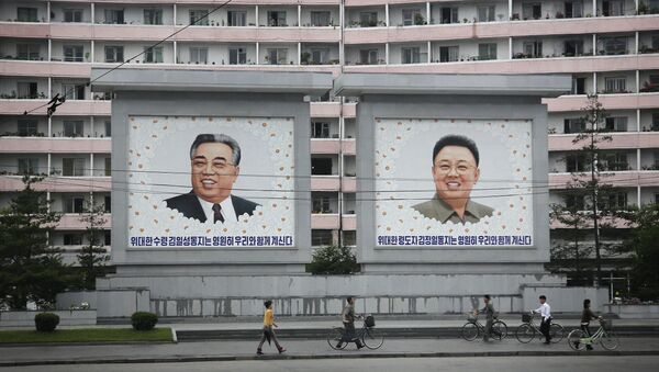 North Koreans are dwarfed against giant portraits of the late North Korean leaders Kim Il Sung and Kim Jong Il as they walk past an apartment building on Wednesday, June 22, 2016, in Wonsan, North Korea. - Sputnik International