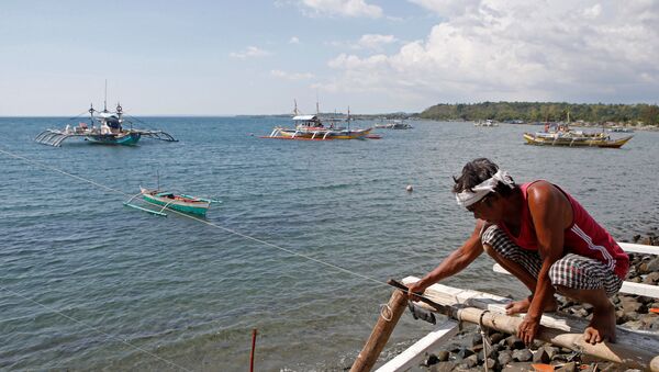 A fisherman repairs his boat overlooking fishing boats that fish in the disputed Scarborough Shoal in the South China Sea, at Masinloc, Zambales,in the Philippines. file photo - Sputnik International