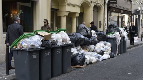 Pedestrians walk past unemptied garbage bins and plastic bags during a strike of garbage collectors in a street in Paris (File) - Sputnik International