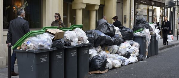Pedestrians walk past unemptied garbage bins and plastic bags during a strike of garbage collectors in a street in Paris (File) - Sputnik International