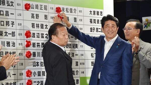 Japanese Prime Minister and ruling Liberal Democratic Party (LDP) president Shinzo Abe (C) places a red paper rosette on an LDP candidate's name to indicate an election victory at the party's headquarters in Tokyo on July 10, 2016 - Sputnik International