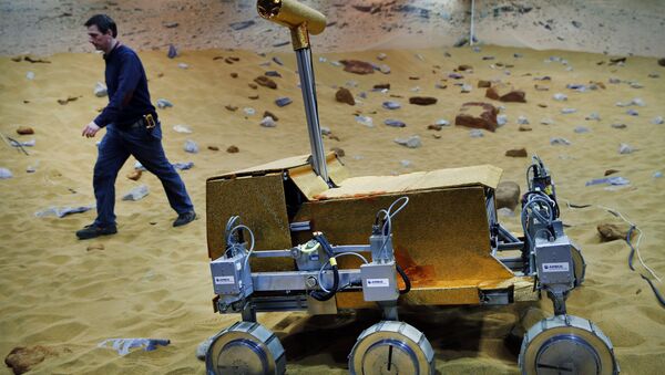 Engineer Ben Nye walks past a robotic vehicle on the 'Mars Yard Test Area', a testing ground for the robotic vehicles of the European Space Agency’s ExoMars program scheduled for 2018, in Stevenage, England, Thursday, March 27, 2014 - Sputnik International