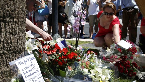 A woman places a bouquet of flowers as people pay tribute near the scene where a truck ran into a crowd at high speed killing scores and injuring more who were celebrating the Bastille Day national holiday, in Nice, France, July 15, 2016. - Sputnik International