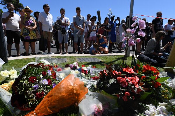 People stand on July 15, 2016 in front of flowers and candles placed near the site in Nice where a gunman smashed a truck into a crowd of revellers celebrating Bastille Day, killing at least 84 people. People stand on July 15, 2016 in front of flowers and candles placed near the site in Nice where a gunman smashed a truck into a crowd of revellers celebrating Bastille Day, killing at least 84 people. - Sputnik International