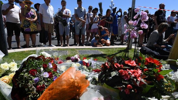 People stand on July 15, 2016 in front of flowers and candles placed near the site in Nice where a gunman smashed a truck into a crowd of revellers celebrating Bastille Day, killing at least 84 people. - Sputnik International