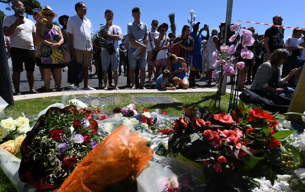 People stand on July 15, 2016 in front of flowers and candles placed near the site in Nice where a gunman smashed a truck into a crowd of revellers celebrating Bastille Day, killing at least 84 people. - Sputnik International