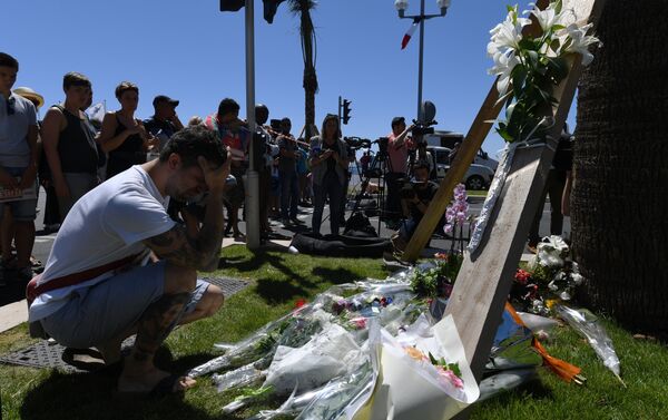 A man kneels and holds his head on July 15, 2016 in front of flowers placed near the site in Nice where a gunman smashed a truck into a crowd of revellers celebrating Bastille Day, killing at least 84 people. - Sputnik International