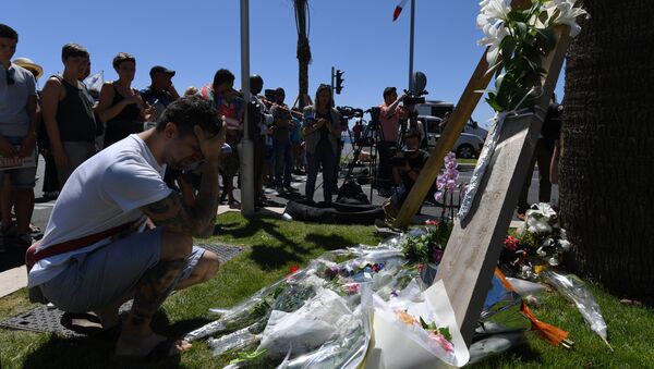 A man kneels and holds his head on July 15, 2016 in front of flowers placed near the site in Nice where a gunman smashed a truck into a crowd of revellers celebrating Bastille Day, killing at least 84 people. - Sputnik International